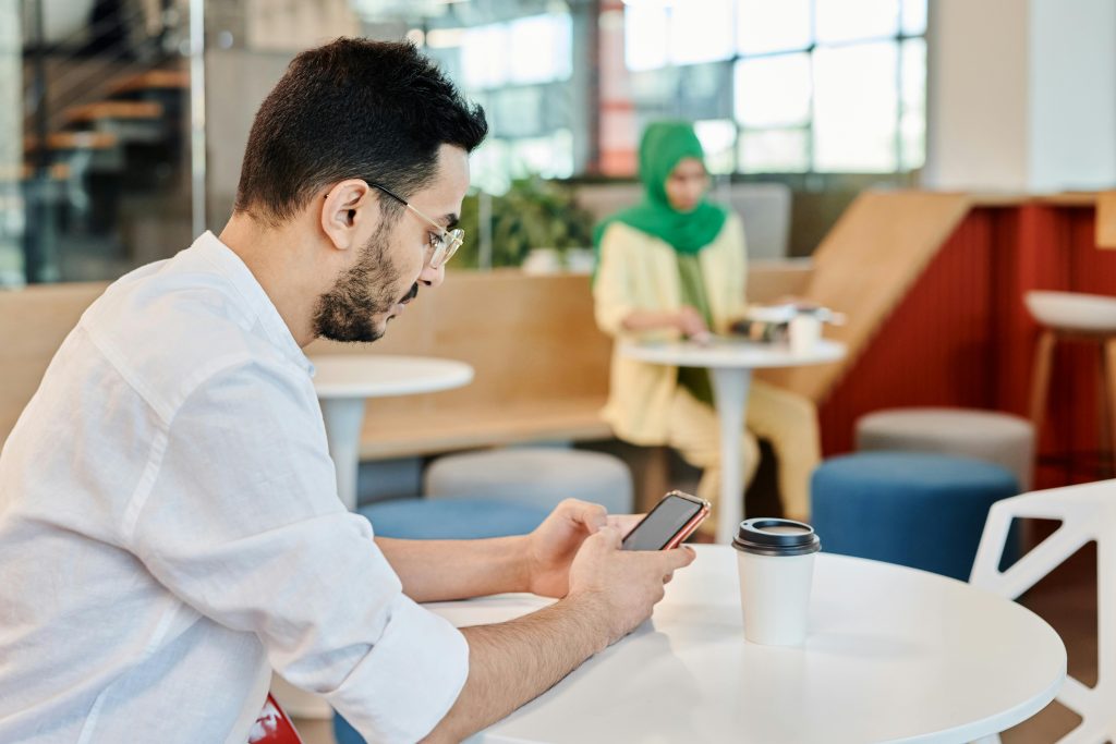 JazzCash vs Easypaisa: Which is Better in Pakistan? (2026 Honest Review) Man in a cafe using a smartphone, drinking coffee, depicting modern lifestyle.