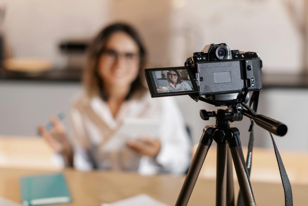 Woman vlogger using a camera and tripod for content creation indoors.